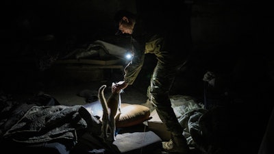 Ukrainian serviceman Anton pets a cat in a basement previously used by Russian soldiers as a temporary base in the village of Malaya Rohan, Kharkiv region, east Ukraine, Monday, May 16, 2022.