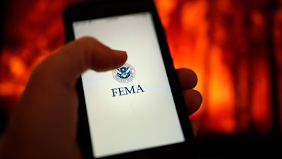 A phone loads the Federal Emergency Management Agency application with the background of an image of a fire on Wednesday, June 29, 2022, in San Diego. FEMA is releasing the largest update to its mobile application in a decade, at the beginning of a hurricane season that experts predict will be above average and a wildfire season that's on par with recent years' big burns.