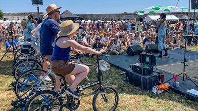 Madi Diaz, right, performs at the Newport Folk Festival's bike stage, powered in part by festivalgoers on stationary bicycles, left, Friday, July 22, 2022, in Newport, R.I.