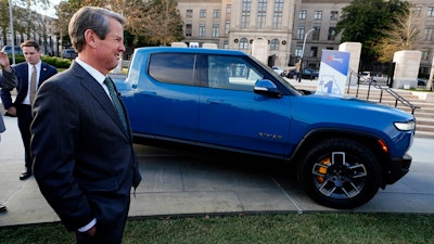 Georgia Gov. Brian Kemp smiles as he stands next to a Rivian electric truck during a ceremony to announce that the electric truck maker plans to build a $5 billion battery and assembly plant east of Atlanta projected to employ 7,500 workers, on Dec. 16, 2021, in Atlanta.