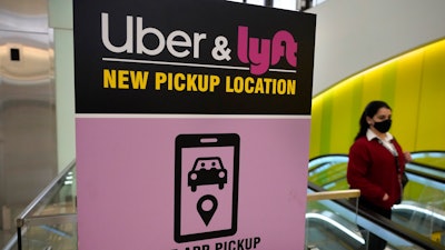 A passerby walks past a sign offering directions to an Uber and Lyft ride pickup location at an airport, Feb. 9, 2021, in Boston.