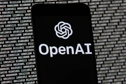 The OpenAI logo appears on a mobile phone in front of a computer screen with random binary data.