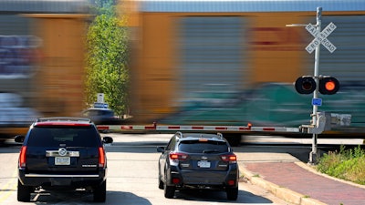 Cars wait at a railroad crossing in Homestead, Pa., as a CSX freight train rolls through.