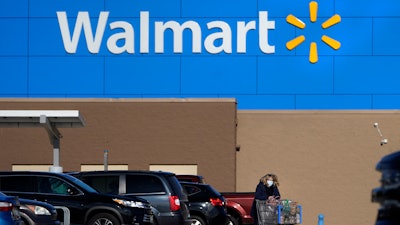 A woman wheels a cart with her purchases out of a Walmart store in Derry, N.H.