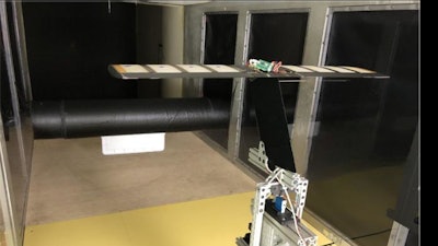 A large black cylinder with a plate attached at the front creates irregular turbulence under the tunnel's high-speed winds. The airfoil wing system with eight pressure sensors and a pitot tube is mounted on a load cell to measure the lift experienced by the system.