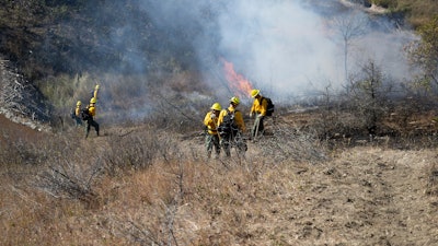 In this photo provided by the U.S. Army National Guard, North Dakota National Guard soldiers and airmen work with the Department of Emergency Services to build a handline and conduct a controlled burn to prevent the further spread of a wildfire in Mandaree, N.D., Oct. 6, 2024.