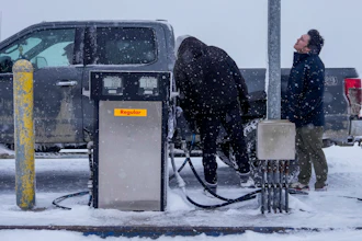 Edwin Solomon, 18, at right, stands in the wind and snow while filling up a truck with regular gas at a price of $7.50 a gallon, Wednesday, Oct. 16, 2024, in Kaktovik, Alaska.
