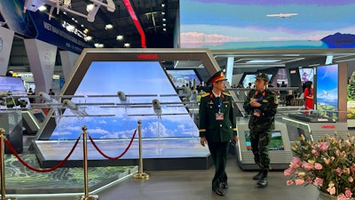 Two men in Vietnamese military uniform talk to each other next to a stall by Vietnamese state-owned firm Viettel at the Vietnam International Defense Expo held in Hanoi, Vietnam, Thursday, Dec.19, 2024.