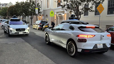 Two Waymo driverless taxis stop before passing one another on a San Francisco street on Feb. 15, 2023.