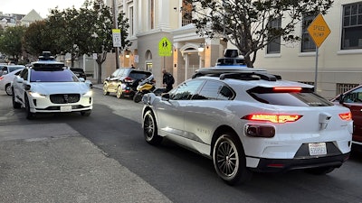 Two Waymo driverless taxis stop before passing one another on a San Francisco street on Feb. 15, 2023.