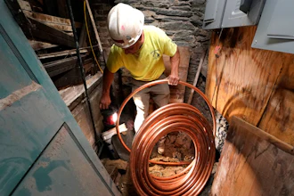 George Philbin, of Boyle & Fogarty Construction, works to feed a new copper residential water supply line, after removing a old lead residential water supply line, in the basement of a home where service was getting upgraded, June 29, 2023, in Providence, R.I.