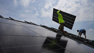 Nicholas Hartnett, owner of Pure Power Solar, carries a panel as he and Brian Hoeppner, right, install a solar array on the roof of a home in Frankfort, Ky., July 17, 2023.