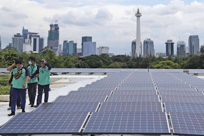 Workers walk near solar panels that provide partial electrical power to Istiqlal Mosque as the city skyline is seen in the background, in Jakarta, Indonesia, Wednesday, March 29, 2023.