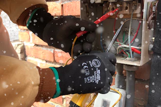 Technician wearing protective gloves repairing electrical panel near brick wall