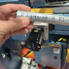 Hand holding labeled industrial cylinder near machinery with voltage indicator