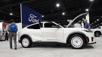 Shoppers look over a 2025 Mach-E electric utility vehicle in the Ford display at the Colorado Auto Show, April 17, 2025, in Denver.