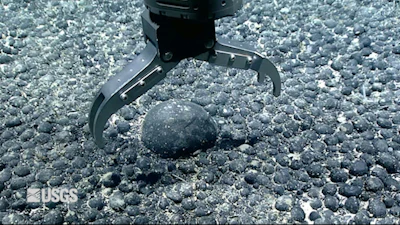 A metal claw reaches for an iron and manganese nodule on the seabed for testing.