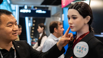 A member of staff touches the face of a humanoid robot showcased at an exhibition in Hong Kong on Monday, April 13, 2026.