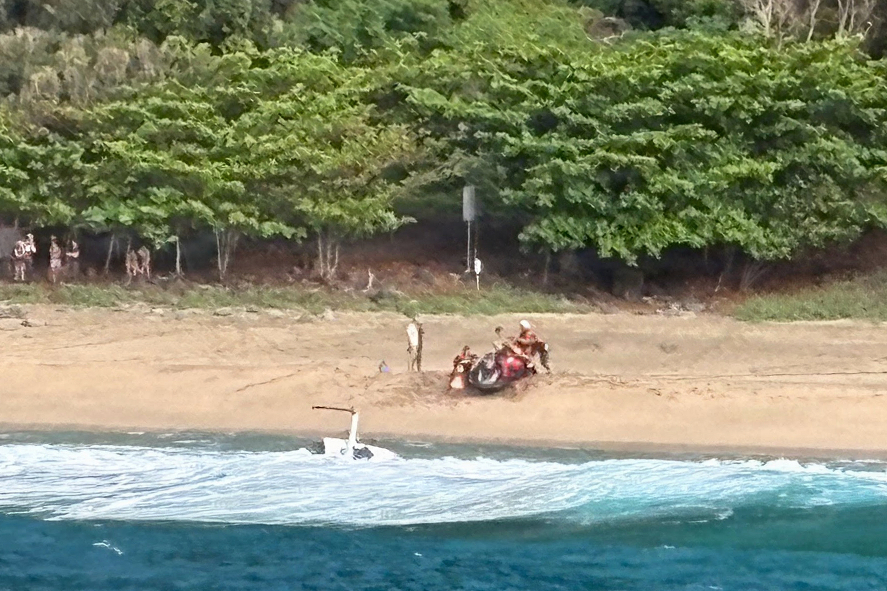 Kauai Ocean Safety members and other people assist individuals after an Airborne Aviation tourist helicopter crash on Kalalau Beach on Kauai, Hawaii, on March 26, 2026.