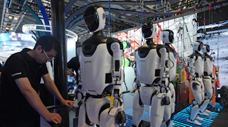A worker reacts near a line of humanoid robots displayed at the World AI Conference in Shanghai, Friday, July 17, 2026.