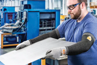 Factory worker in safety glasses and protective gloves inspecting white material at workstation with blue industrial machinery in background