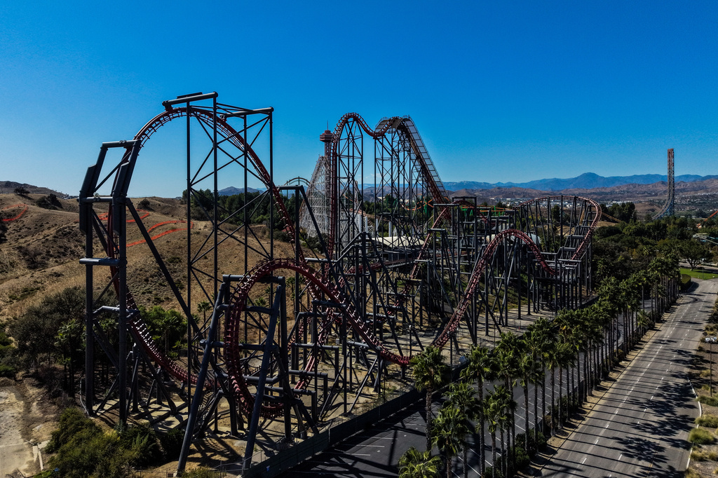 Aerial view of a steel roller coaster with red tracks winding through desert landscape and mountains in background