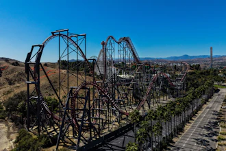 Aerial view of a steel roller coaster with red tracks winding through desert landscape and mountains in background