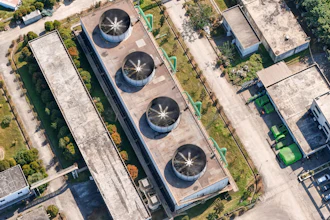 Aerial view of industrial facility with four circular cooling towers on rooftop surrounded by landscaped grounds and adjacent buildings