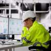 Construction worker in safety gear analyzing data charts on computer monitor in industrial facility
