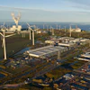 Aerial view of industrial port facility with wind turbines, warehouses, and waterways along coastal landscape