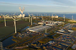Aerial view of industrial port facility with wind turbines, warehouses, and waterways along coastal landscape