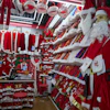 Christmas market stall displaying red Santa costumes, white fur trim, and holiday decorations with a young shopper browsing merchandise.
