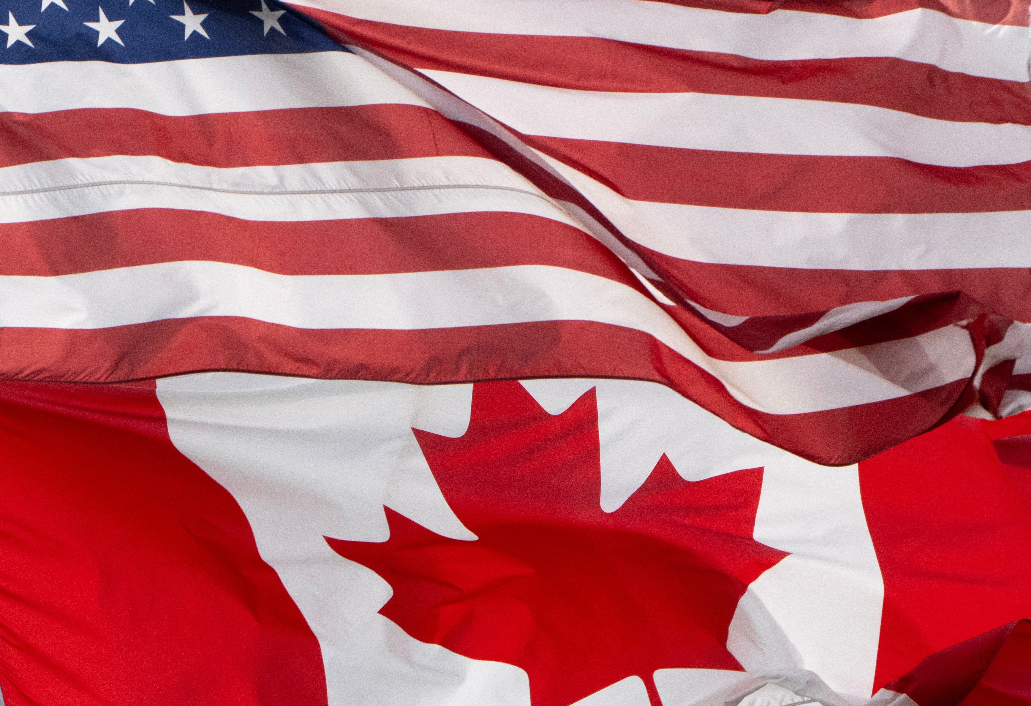 United States and Canadian flags overlapping, showing red and white stripes with stars and maple leaf symbols