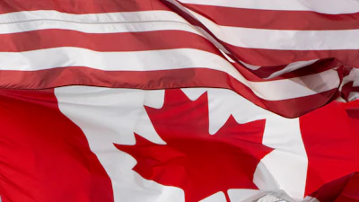 United States and Canadian flags overlapping, showing red and white stripes with stars and maple leaf symbols