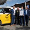 Five men pose with yellow Volkswagen Giti electric commercial vehicle and Guinness World Record certificate at outdoor event