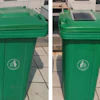 Two green recycling bins with white circular emblems on a paved outdoor surface