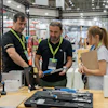 Trade show booth demonstration with staff and visitors examining tools and equipment at an industrial exhibition