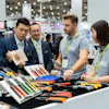 Professionals examining tools and equipment at a trade show booth with green lanyards