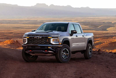 Silver Chevrolet Silverado pickup truck parked on desert terrain with mountains in background