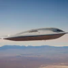 Futuristic silver aircraft with streamlined design flying over desert landscape and distant mountains