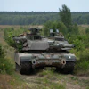 Military tank positioned in forested terrain with coniferous trees and cleared ground in background