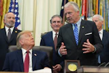 Formal meeting in the Oval Office with government officials and American flags in background