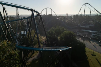 Aerial view of blue roller coaster tracks winding through an amusement park surrounded by trees and landscape