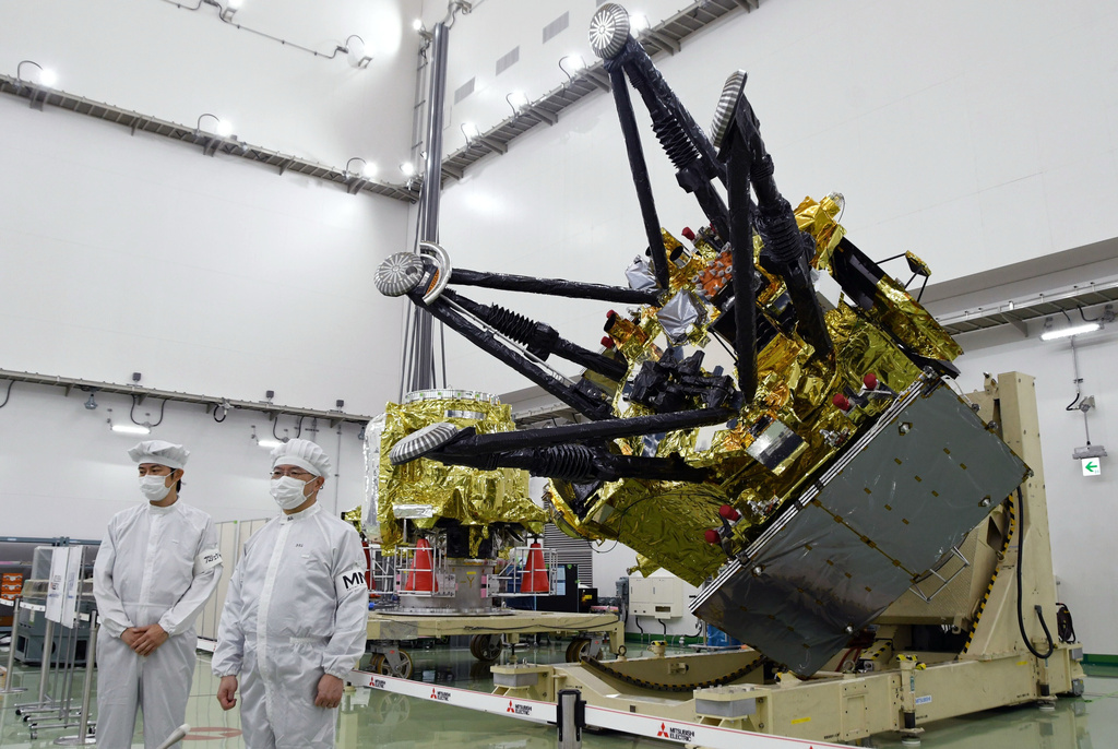 Satellite component with gold thermal insulation and black mechanical arms in clean room facility with technicians in protective suits
