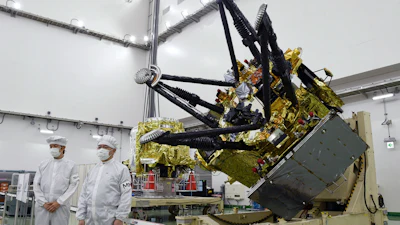 Satellite component with gold thermal insulation and black mechanical arms in clean room facility with technicians in protective suits