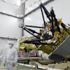 Satellite component with gold thermal insulation and black mechanical arms in clean room facility with technicians in protective suits