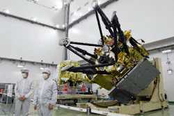 Satellite component with gold thermal insulation and black mechanical arms in clean room facility with technicians in protective suits