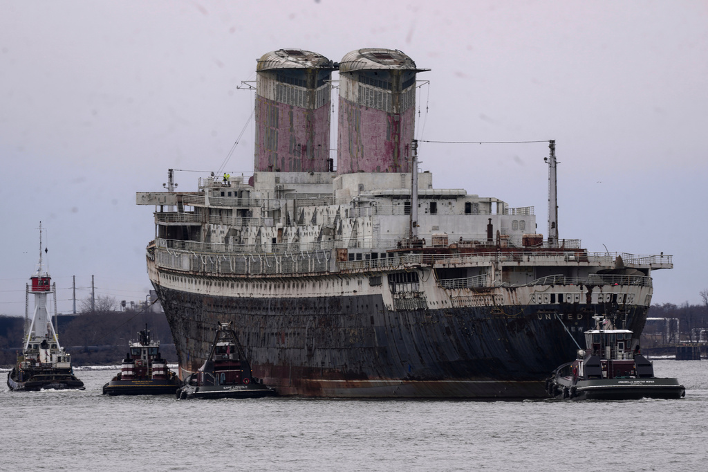 Large cargo ship assisted by tugboats in port waters with industrial twin smokestacks visible