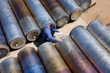 Worker in blue surveying large industrial metal pipes arranged on sandy ground from above