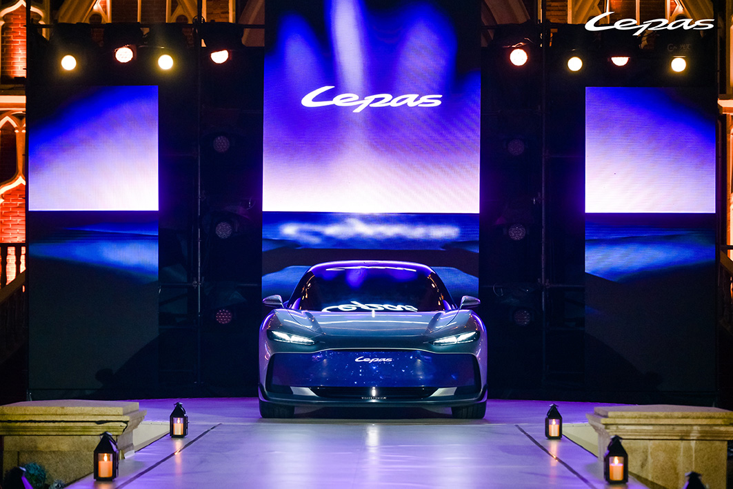 Luxury sports car displayed on stage during brand launch event with illuminated screens and dramatic blue lighting